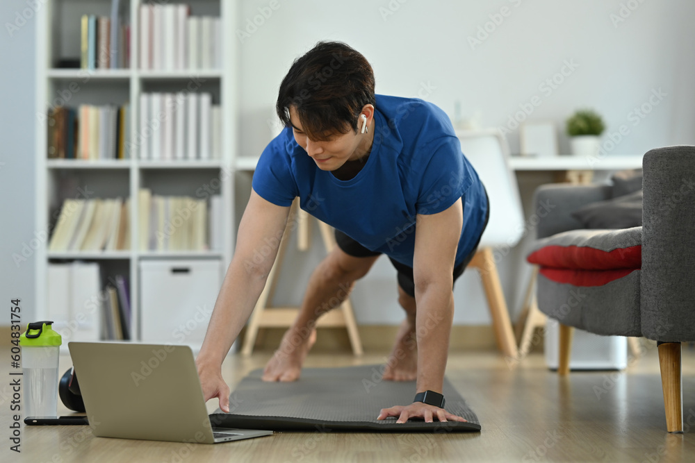 Young man in sportswear working out at home and watching fitness lessons online on laptop. Fitness, training and healthy lifestyle