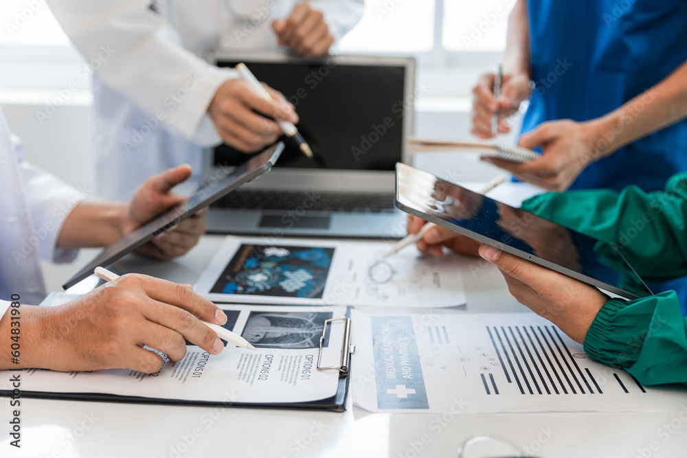 © Witoon - Medical team meeting with doctors in white lab coats and surgical gowns sitting at table discussing patient history. success of medical health care The concept of working with a doctor. Close up.