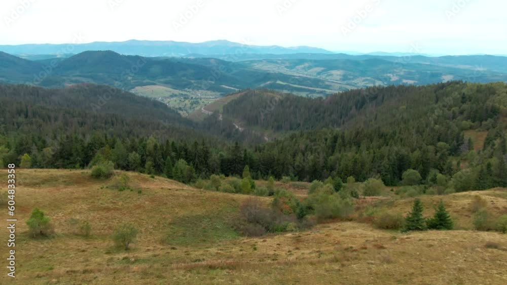 Drone view over Carpathian mountain peak passing man in yellow rain coat admiring nature. Wide shot aerial view of Ukrainian landscape on cloudy morning outdoors