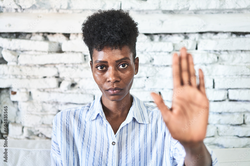 A miggle-aged african woman sitting on her sofa standing with outstretched hand showing stop sign, preventing you. A miggle-aged african woman sitting on her sofa standing with outstretched hand showing stop sign, preventing you.