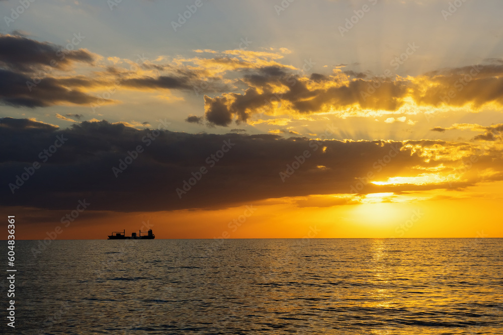Silhouette of a fishing vessel during sunset at sea. Beautiful color photo, the sun behind the clouds.