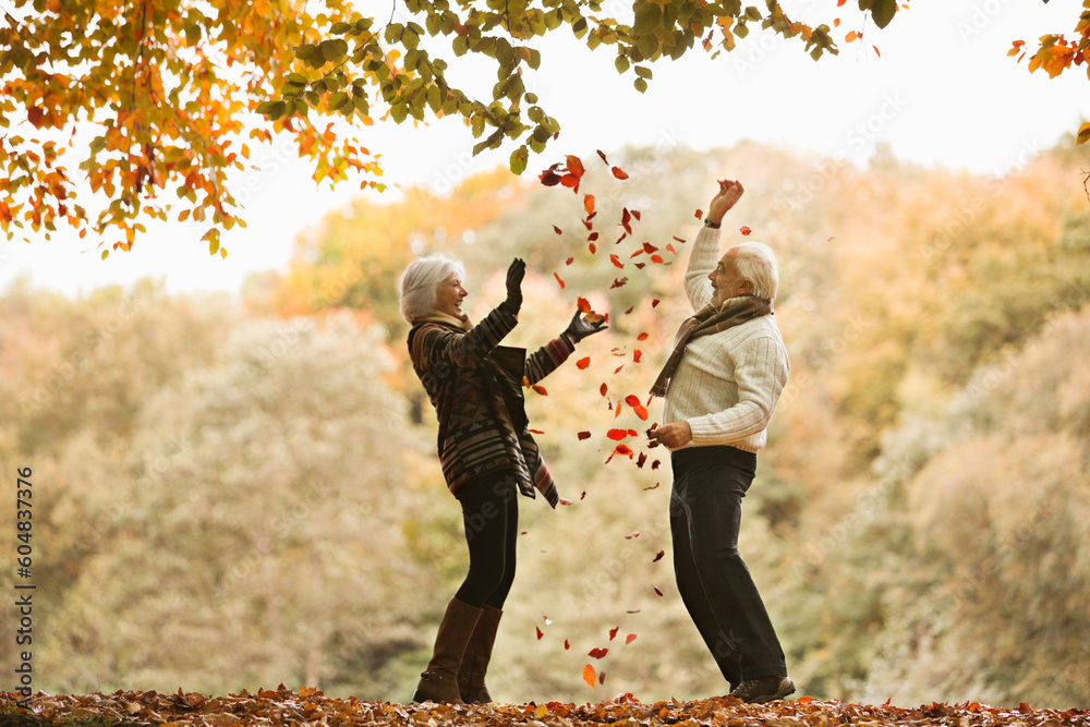 Older couple playing in autumn leaves - obrazy, fototapety, plakaty 
