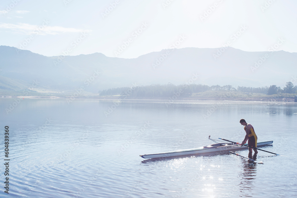 Naklejka premium Man placing rowing scull in lake