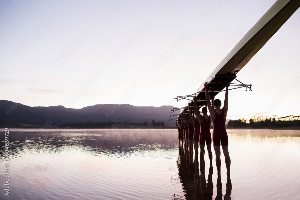 Rowing team entering lake at dawn with scull overhead  - obrazy, fototapety, plakaty 
