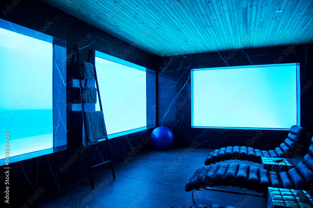 Lounge chairs in pool room facing windows underwater view of swimming