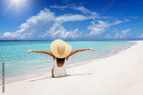 A happy woman in a white bathing suit sits on a tropical beach and enjoys her summer vacation time #604840144