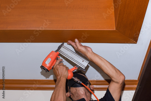 Man hand holding electric nail gun (pneumatic gun) repair ceiling at home.