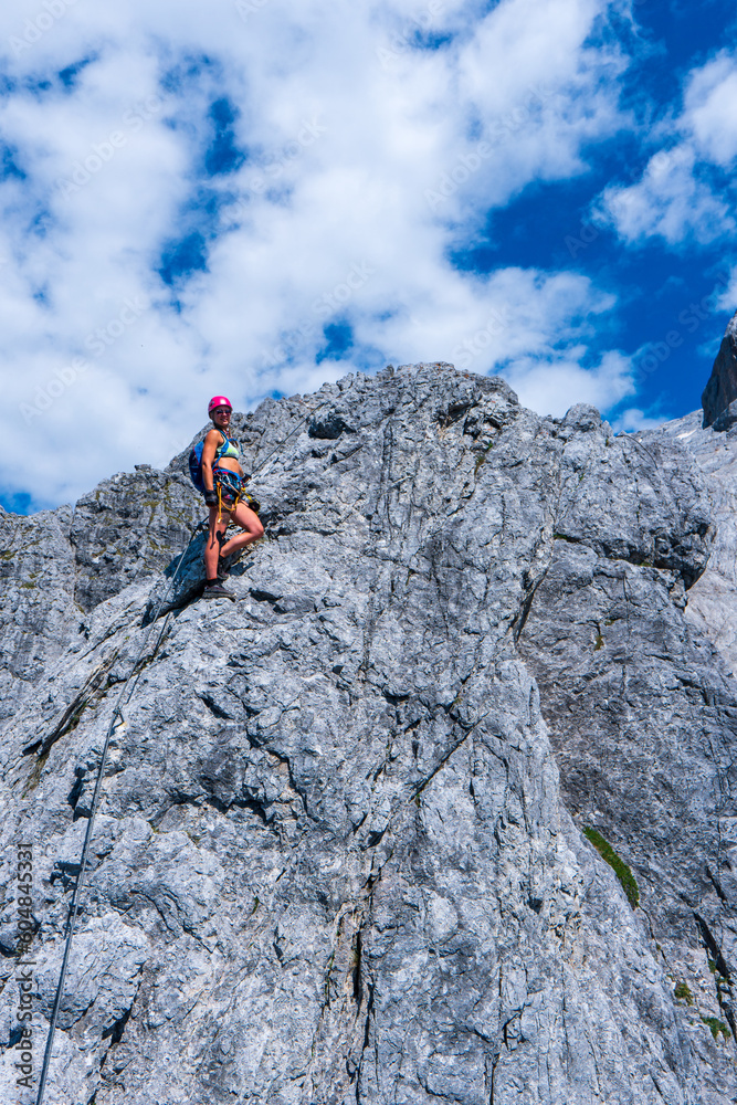 Young woman with backpack climbing along sharp alpine ridge