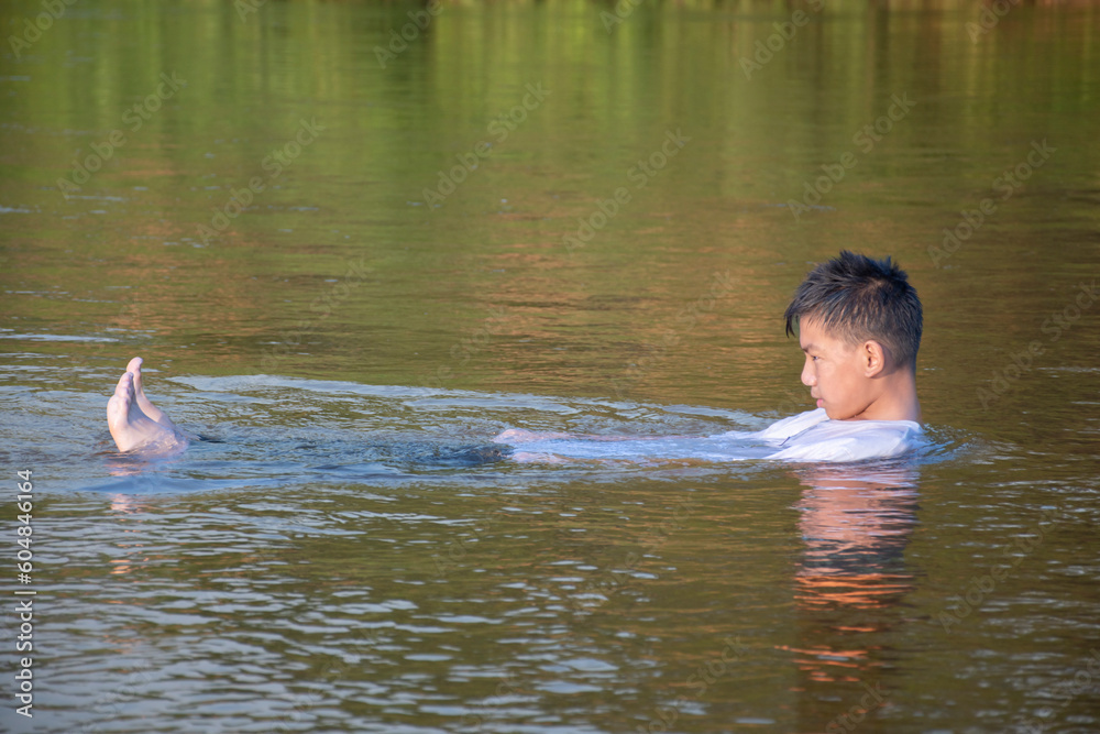 Fototapeta premium Asian boy in white t-shirt is spending his freetimes by diving, swimming, throwing rocks and doing masturbation in the river happily, hobby and happiness of children concept, in motion.