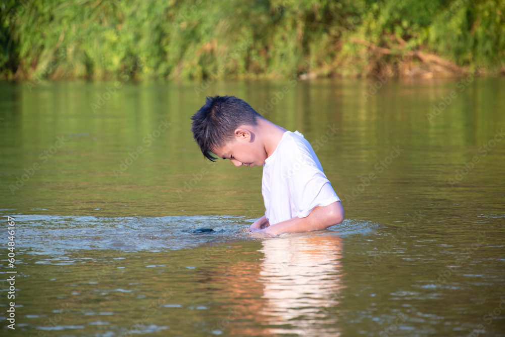 Fototapeta premium Asian boy in white t-shirt is spending his freetimes by diving, swimming, throwing rocks and doing masturbation in the river happily, hobby and happiness of children concept, in motion.