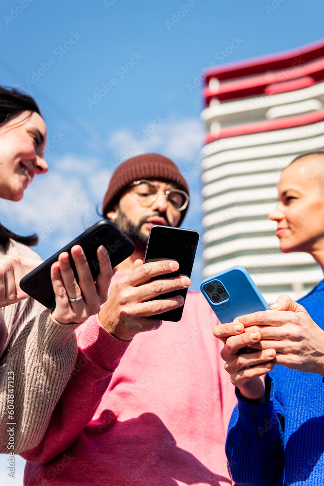 Fototapeta premium three young friends having fun using mobile phones at city, focus on the hands, concept of modern urban lifestyle and technology of communication, copy space for text