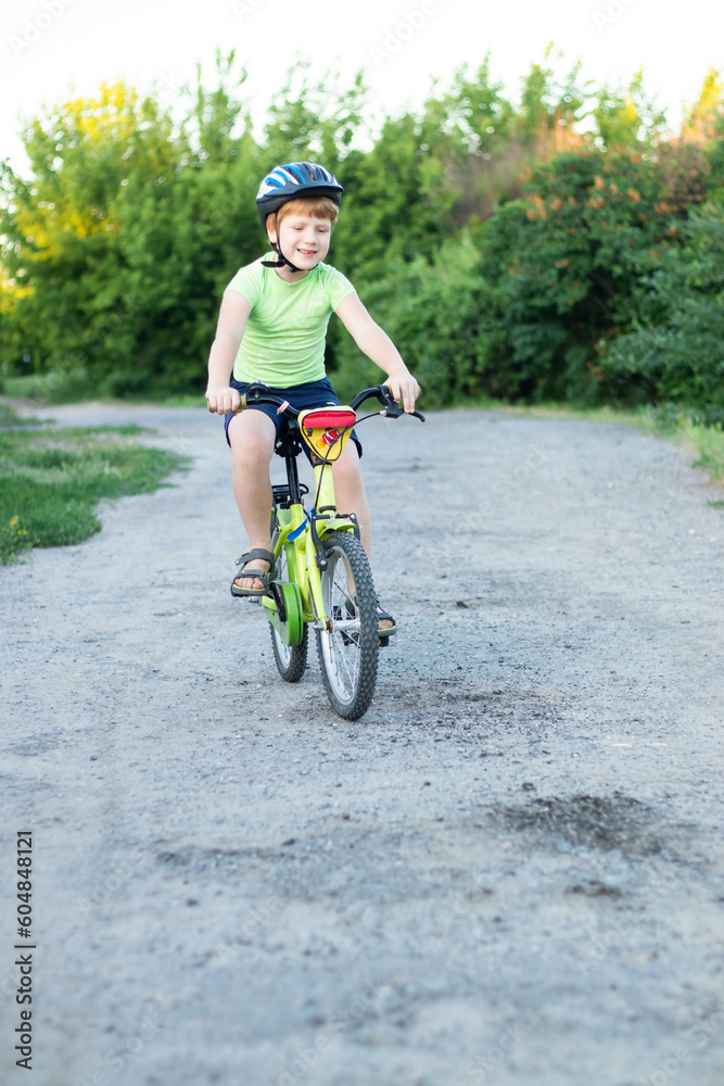 Fototapeta premium teenager boy in helmet and green T-shirt riding a bike on the gravil road in summer