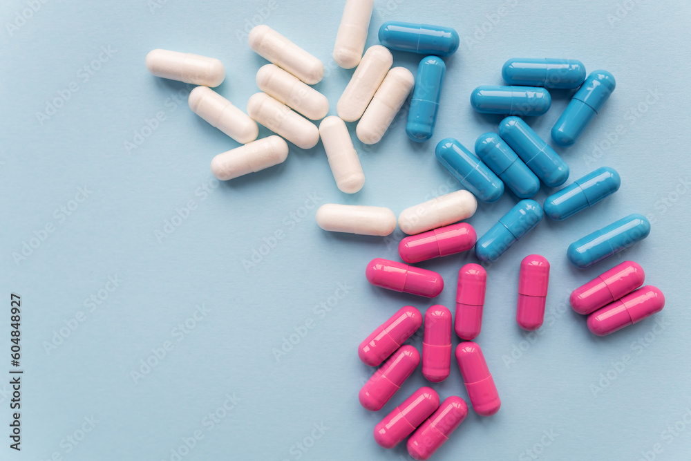 Various colored pills - blue, pink, white, falling out of a plastic bottle, isolated on a blue background. Various colored pills - blue, pink, white, falling out of a plastic bottle, isolated on a blue background.