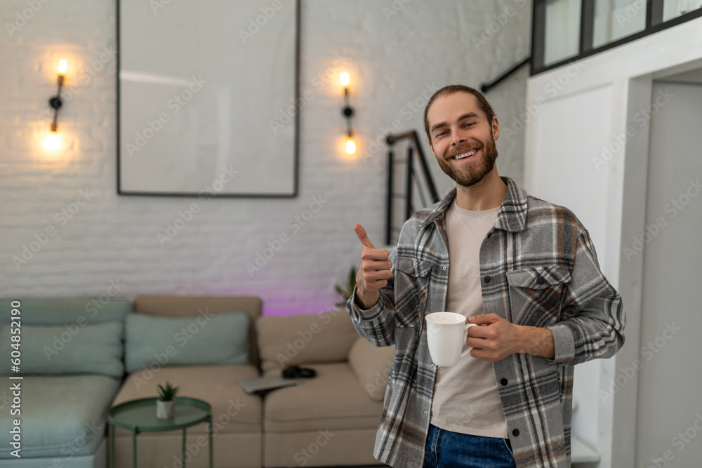 Man holding cup of coffee or tea in hands enjoying free time with hot beverage, showing thumb up
