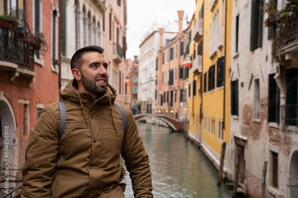 Young tourist man with beard on the canals of Venice among colorful facades