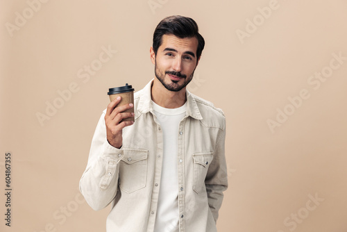 Portrait of a stylish man smile with a cup of coffee to go mock up on a beige background in a white t-shirt, fashionable clothing style, space space