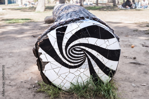 Mosaic trunk  a tiles decoration at a tree trunk in a park. Hippy and abstract wood art design. Spiral shape in black and white pattern. Street decor.