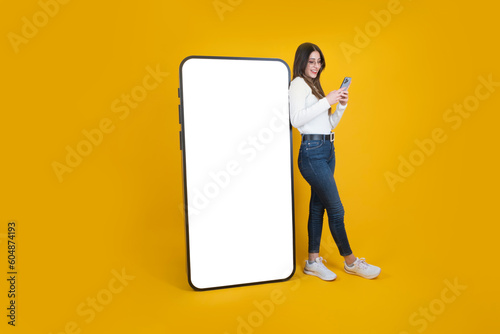 Woman leaning big smartphone, full body view woman leaning big smartphone. Using mobile phone, standing over isolated yellow background. Huge modern phone mockup. Recommending app, website, copy space photo
