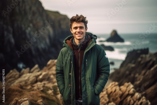 Environmental portrait photography of a joyful boy in his 30s wearing a cozy winter coat against a dramatic coastal cliff background. With generative AI technology