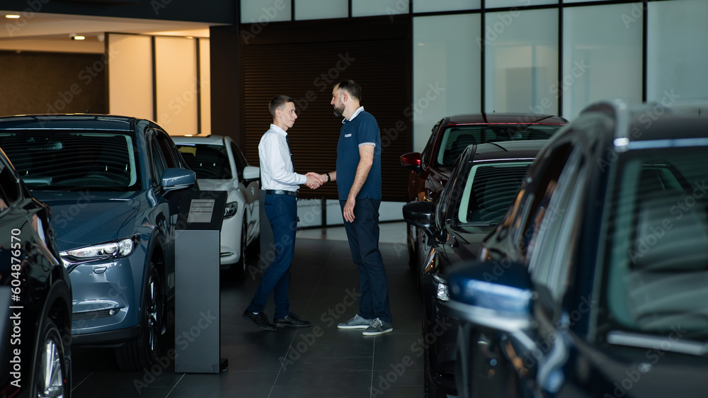 Seller and buyer shake hands in a car dealership. Caucasian man buys a car. Seller and buyer shake hands in a car dealership. Caucasian man buys a car.