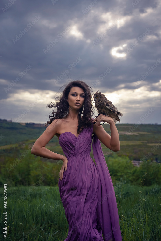 Obraz premium Beautiful woman with owl in purple dress in nature