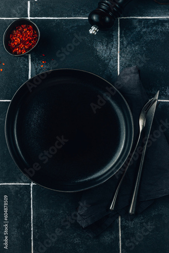 Empty black plate over dark tile background with free space. Top view