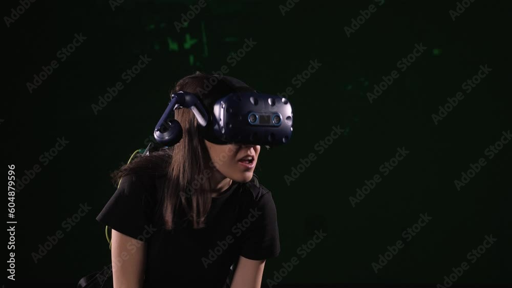 A woman in virtual reality glasses with a joystick in her hands is playing a virtual game on a black background. A gamer girl shoots from a machine gun in a virtual reality game studio. A woman in virtual reality glasses with a joystick in her hands is playing a virtual game on a black background. A gamer girl shoots from a machine gun in a virtual reality game studio.