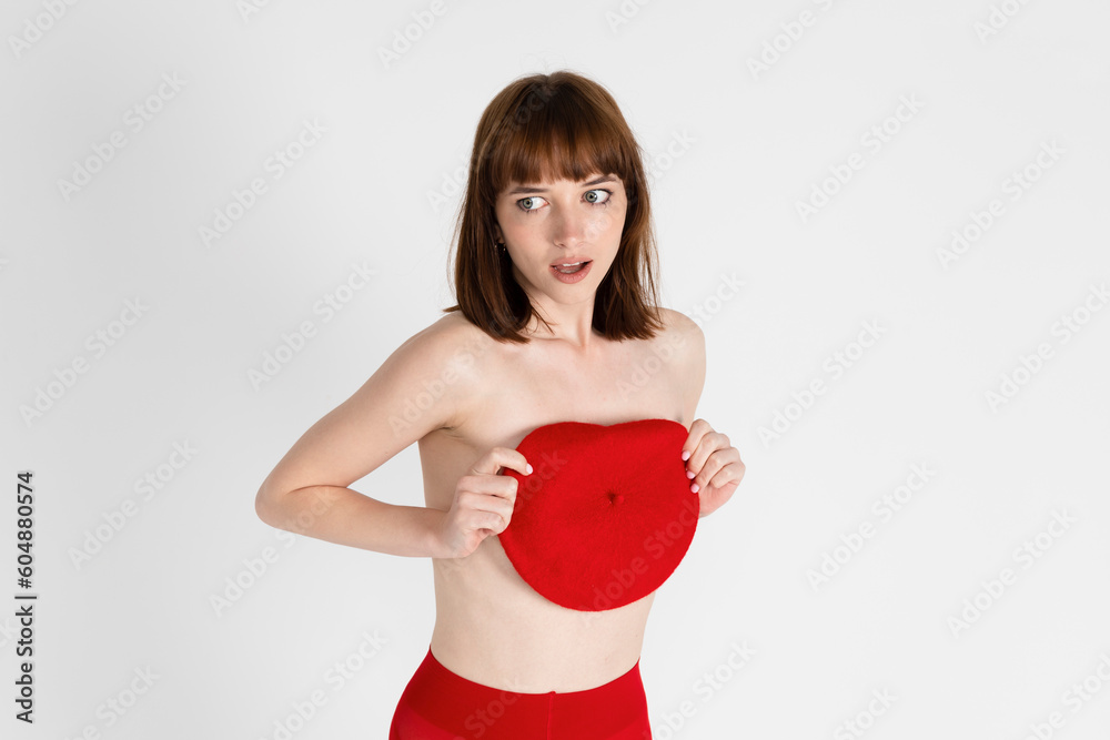 Young beautiful girl only in red tight and a beret, covering her bare chest. Sensual slim girl posing topless. Isolated on white background. Young beautiful girl only in red tight and a beret, covering her bare chest. Sensual slim girl posing topless. Isolated on white background.