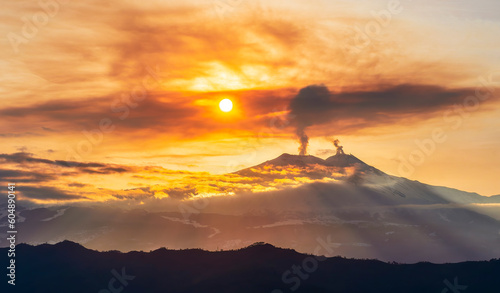 mysterious landscape of great erupting volcano with smoke from craters and snow on slopes in orange light of sunset. eruption of vulcan photo