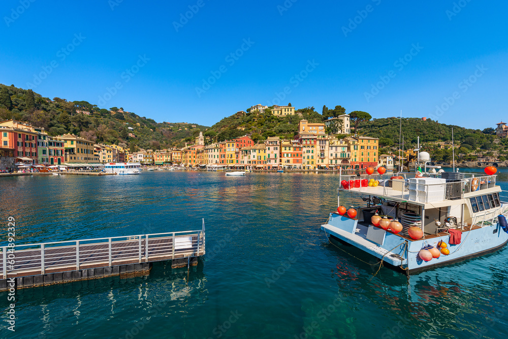 Wooden pier and a fishing boat moored in the famous port of Portofino, luxury Tourist resort in Genoa Province, Liguria, Italy, Europe. Colorful houses, Mediterranean sea (Ligurian sea). - obrazy, fototapety, plakaty 