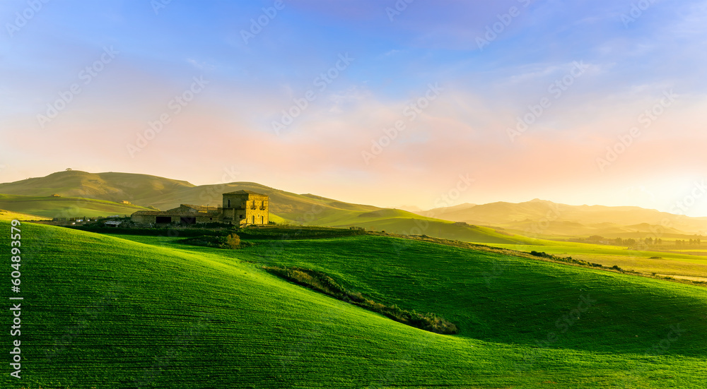 sceniv view at a nice farm in green fields in hills and highlands, landscape of spring green hills with mountain bright sunset on backdrop
