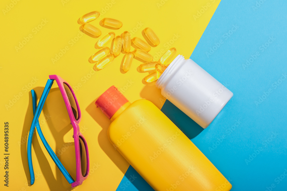 A tube of sunscreen, sun protection pills and sunglasses on a blue and