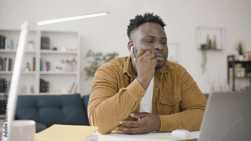 Naklejka premium African American man watching a video or having online conference call with wireless earbuds in his ears, enjoying new device