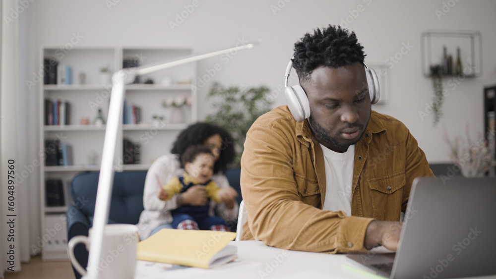 African American man working on laptop in headphones while mother is trying to comfort crying baby African American man working on laptop in headphones while mother is trying to comfort crying baby