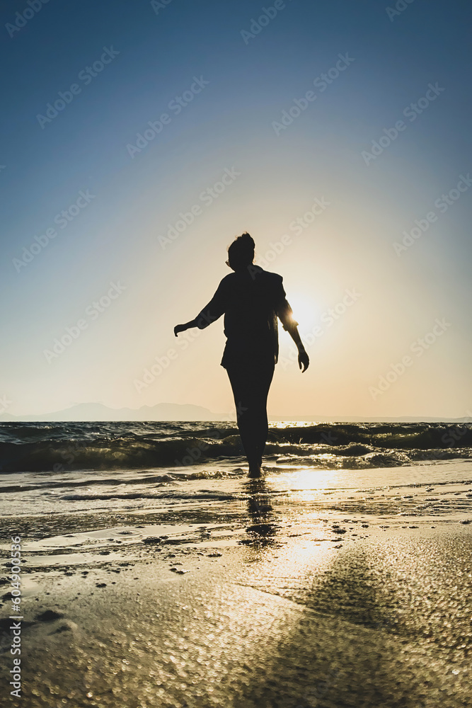 Low angle view of woman walking in backlit on a beach at sunset.