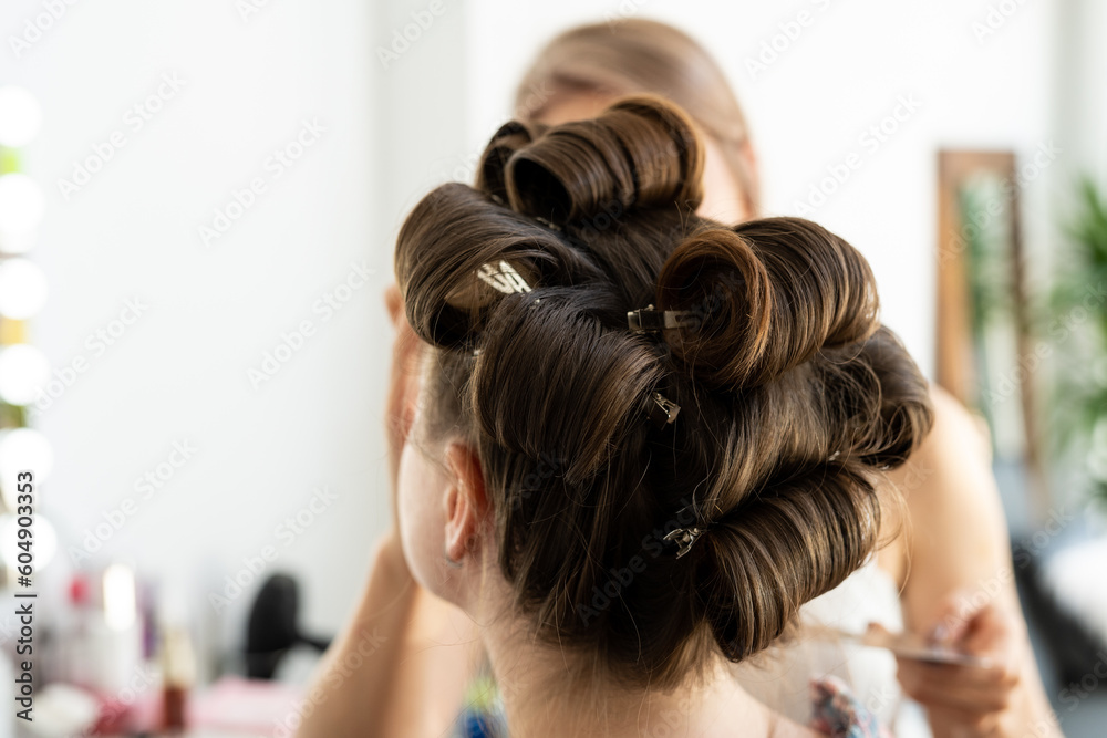 Fototapeta premium The hairdresser curls the model's hair. Curling iron for curling hair close-up.