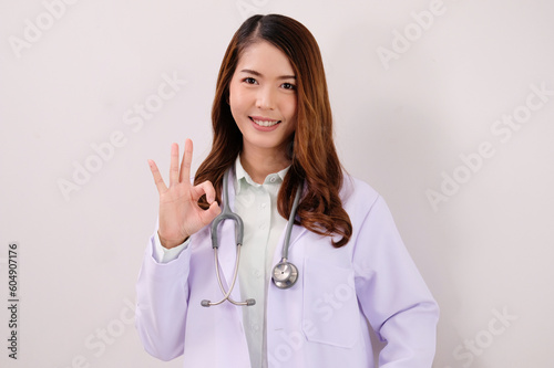 Smiling Asian female doctor raising hands showing OK sign on a white background