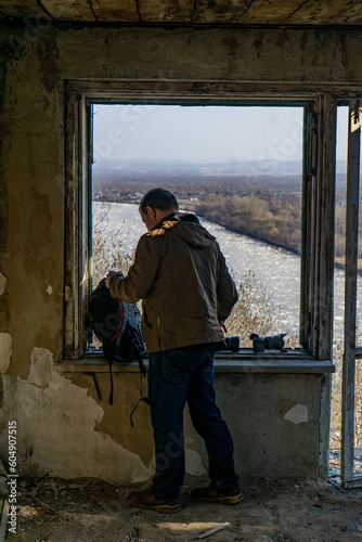 A man in a green jacket looks out the window of an abandoned building.