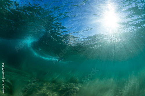 underwater wave crashing with sun rays and a surfer