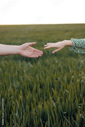 Young man and woman holding hands outdoors on the background of a green field at summer or spring. close-up, vertical picture. A couple, a girl and a boy, bride and groom