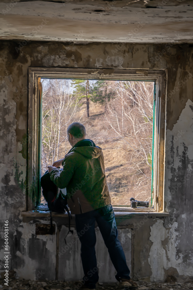 A man in a green jacket looks out the window of an abandoned building. A man in a green jacket looks out the window of an abandoned building.