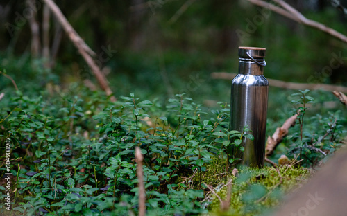 Steel water bottle in forest. Eco friendly travel concept. Hiking with reusable water source. No plastic concept.
