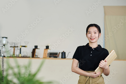 Portrait of smiling young cafe waitress holding wooned board for sushi serving
