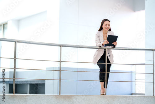 Portrait adult Asian business woman wearing suit holding and Using Digital Tablet Computer at office building