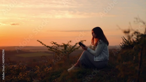 A girl reads the Bible in the open air. A woman holds a Bible in her hands and studies the word of God while sitting in a field at sunset