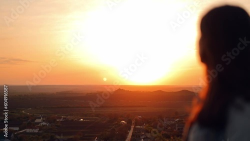 Beautiful young woman reading the bible while standing on top of a hill with a beautiful view at sunset, admiring the view and nature, relaxing alone with thoughts