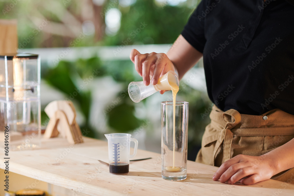Barista pouring condensed milk in tall glass when making cold coffee