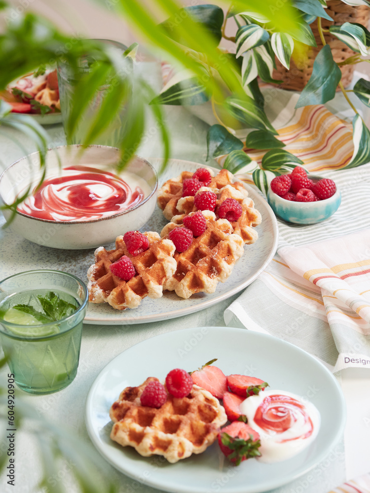 waffles with fresh raspberries on top served on plate with bowl of yogurt waffles with fresh raspberries on top served on plate with bowl of yogurt