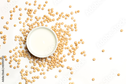 Leche de soja en un cuenco blanco junto a granos esparcidos de soja sobre un fondo blanco liso. Vista superior y de cerca. Copy space