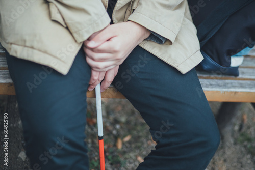 コートを着た視覚障害者の男性が白杖を持って休んでいる